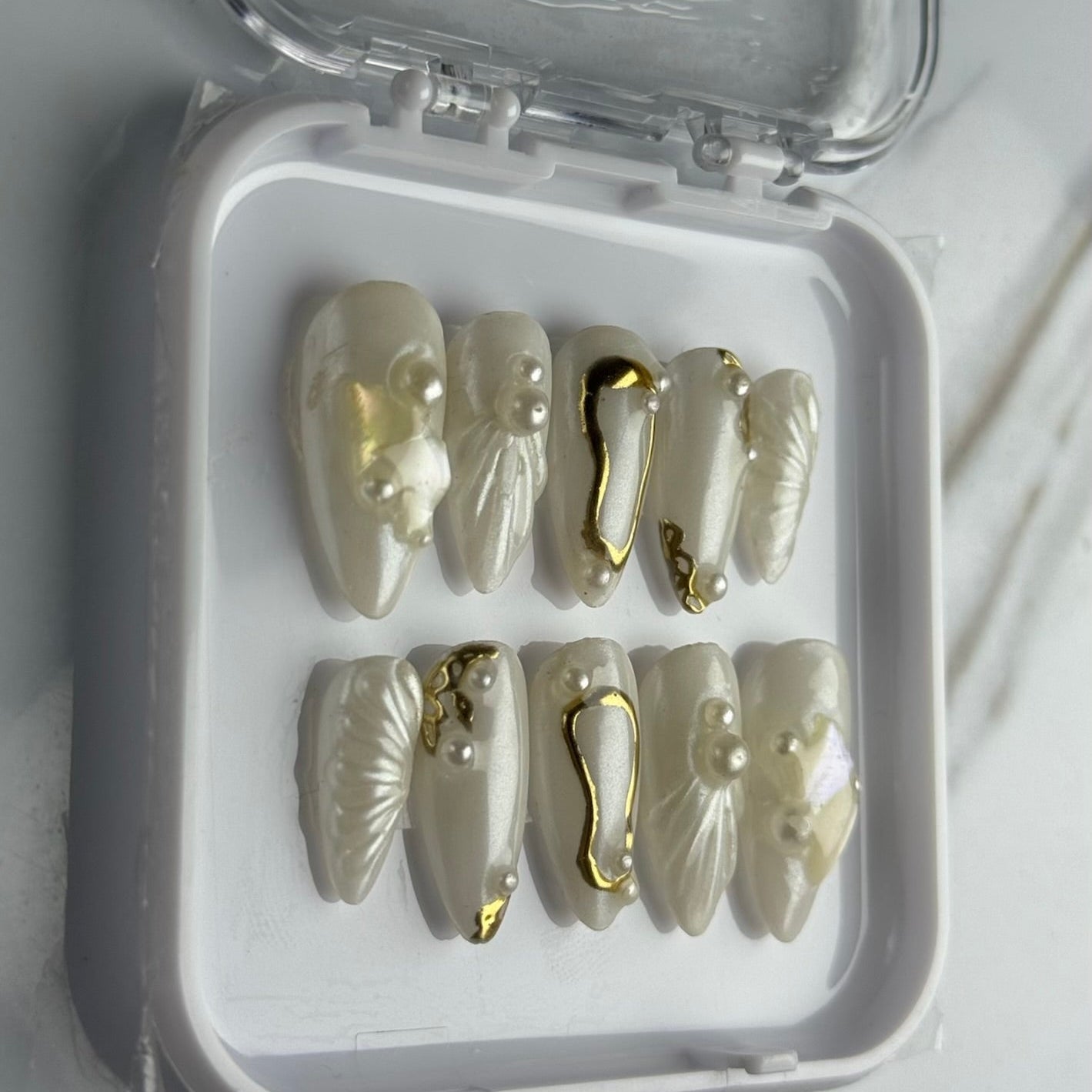 Set of decorative nails with gold accents in a clear container on a white background