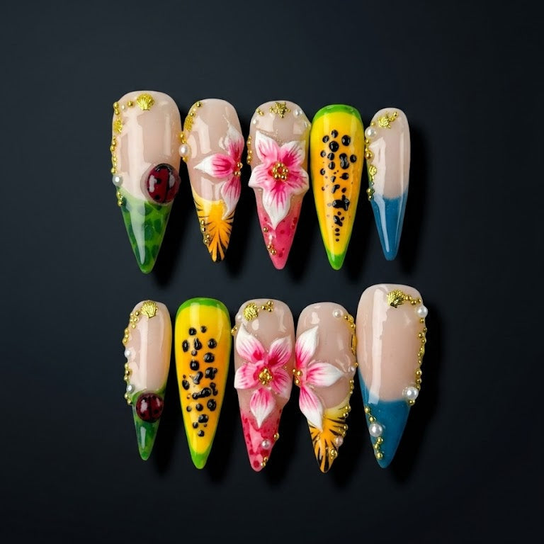 Tropical press-on nails with pink hibiscus flowers, papaya-inspired nail art, blue French tips, pearl embellishments, and gold details.
